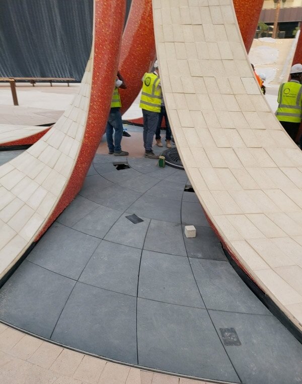 Montage de dallage en pierre autour d'une sculpture en arc à l'expo 2020
