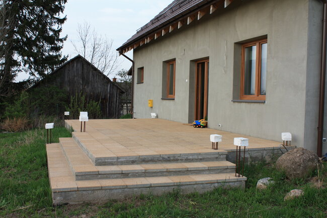 Taras z jasnych płyt betonowych ze schodami w trakcie wykończenia