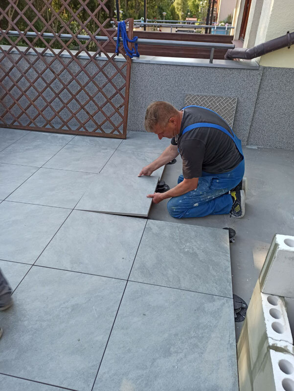 Professionnel posant des dalles en grès cérame grises sur plots de terrasse