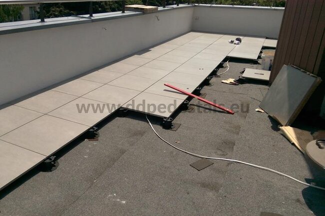 Photo de montage d'une terrasse surélevée sur plots avec utilisation de dalles.