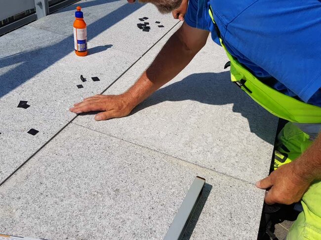 Un homme posant des dalles de terrasse sur des plots réglables solver sur une terrasse