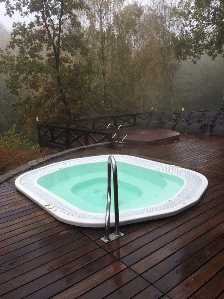Jacuzzi de jardin intégré sur une terrasse en bois entourée de forêt.