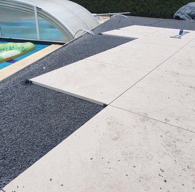 Pose de dalles de terrasse claires sur plots sur un lit de gravier près de la piscine.