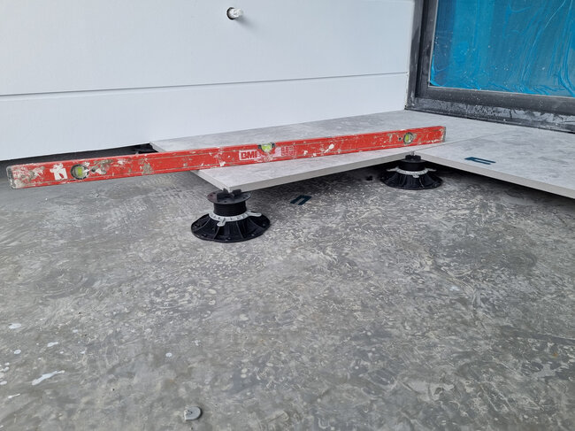 Contrôle du niveau des dalles en grès cérame posées sur plots de terrasse.