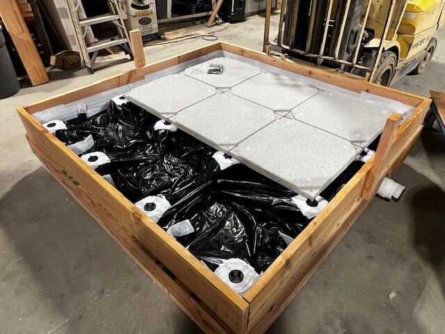 Grand cadre en bois avec plot, doublure en plastique noir et dalles de terrasse en porcelaine gris clair installées sur un toit
