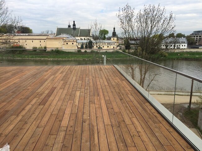 Terrasse en bois surélevée résistante au vent sur un toit avec garde-corps en verre surplombant le quai fluvial