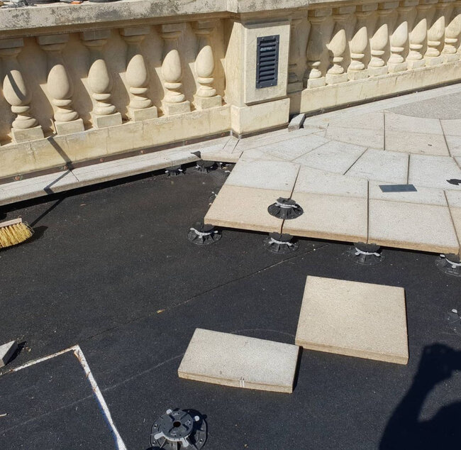 Installation de dalles en pierre extérieures sur plots en plastique réglables sur une membrane d'étanchéité de toit noire.