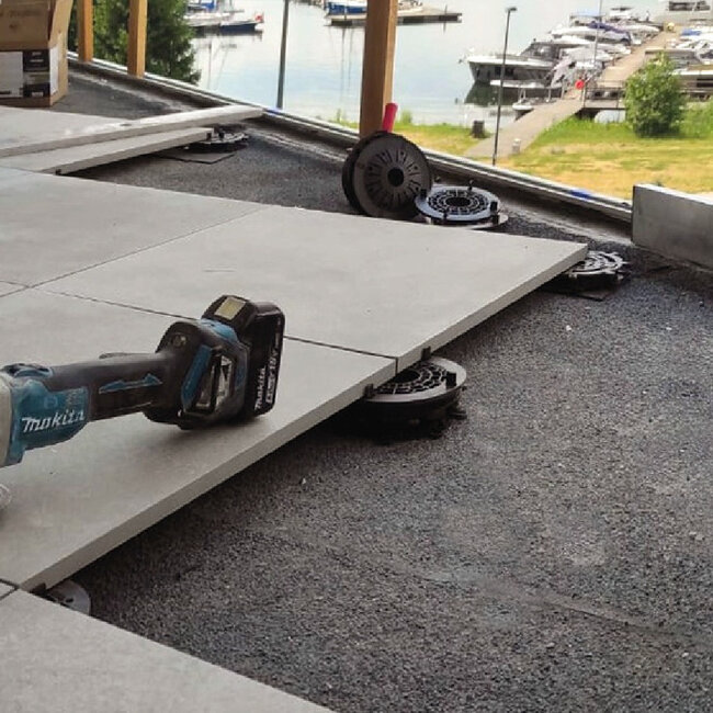 Installation de dalles de terrasse extérieures en porcelaine sur des plots réglables en plastique à profil bas à l'aide d'un outil électrique sans fil.