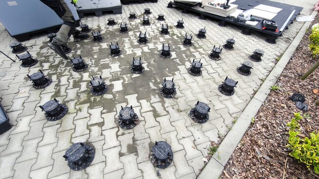 Disposition en grille de plots réglables en plastique placés sur des pavés pour l'installation d'une terrasse extérieure