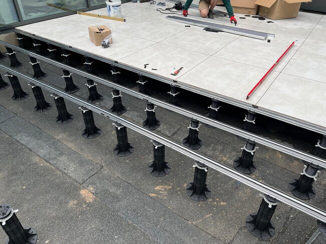 Installation d'une terrasse extérieure surélevée à l'aide de plots réglables en plastique et de lambourdes porteuses en aluminium avec des dalles en céramique.