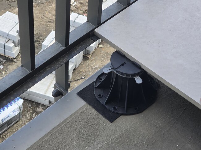 Plot en plastique réglable supportant une dalle en porcelaine le long du bord d'un balcon.