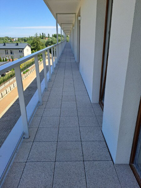 Revêtement de terrasse extérieure long terminé avec des dalles de terrasse à texture béton et des garde-corps blancs.
