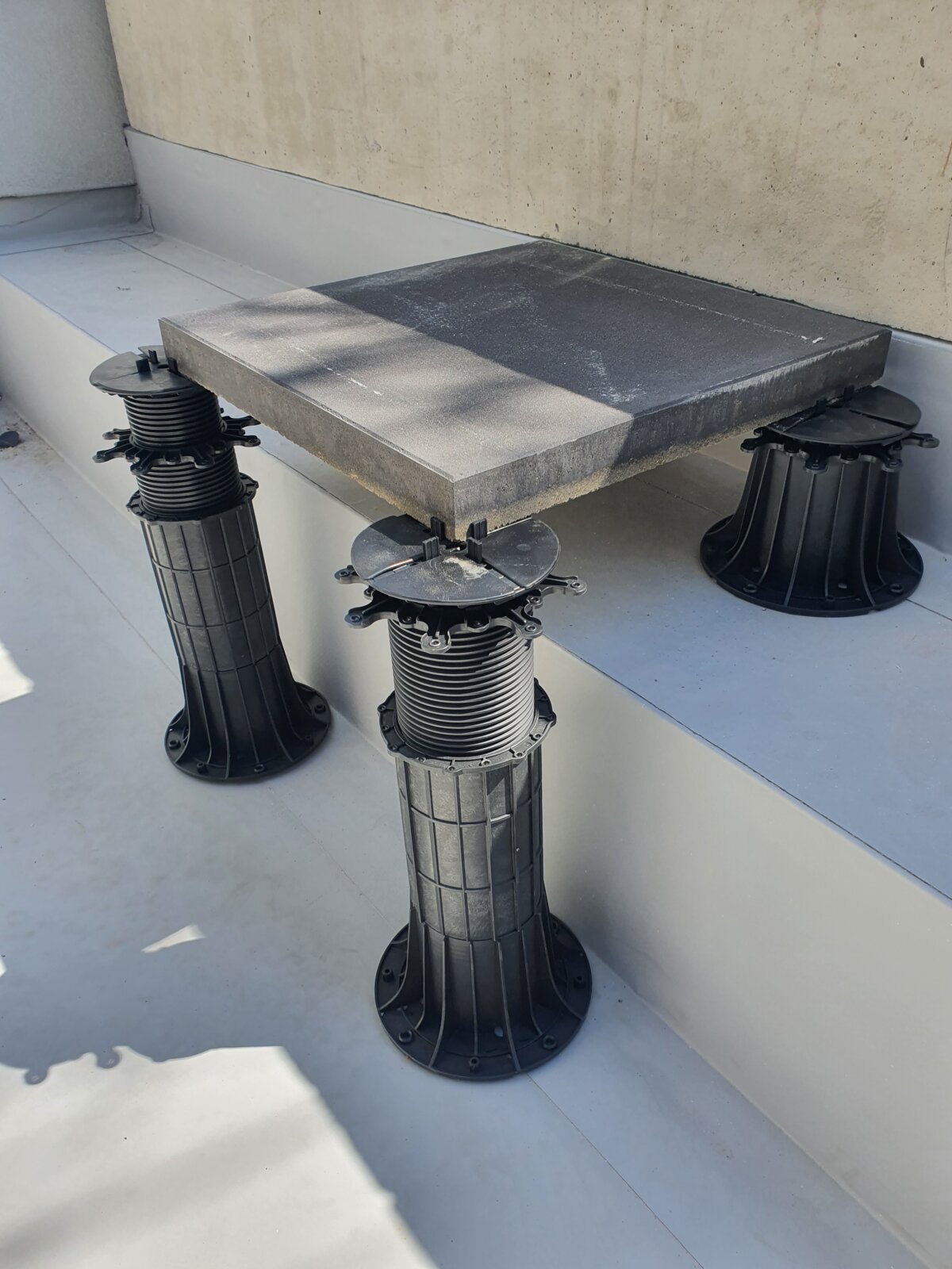 Dalle en béton carrée montée sur des plots en plastique réglables.
