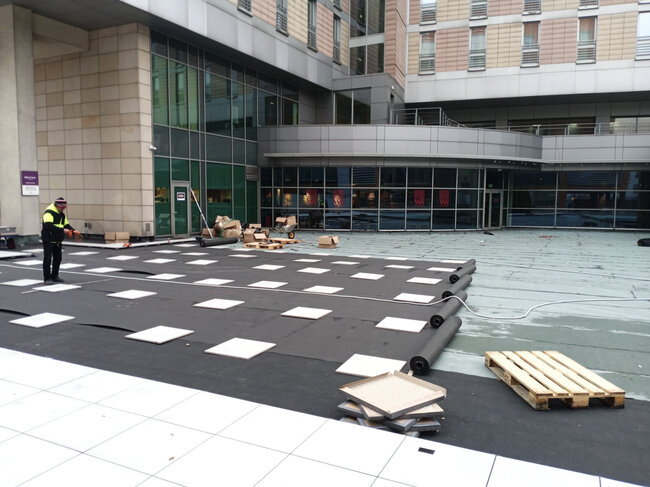 Ouvrier du bâtiment installant des plots de terrasse et une membrane de base sur le toit d'un bâtiment commercial.