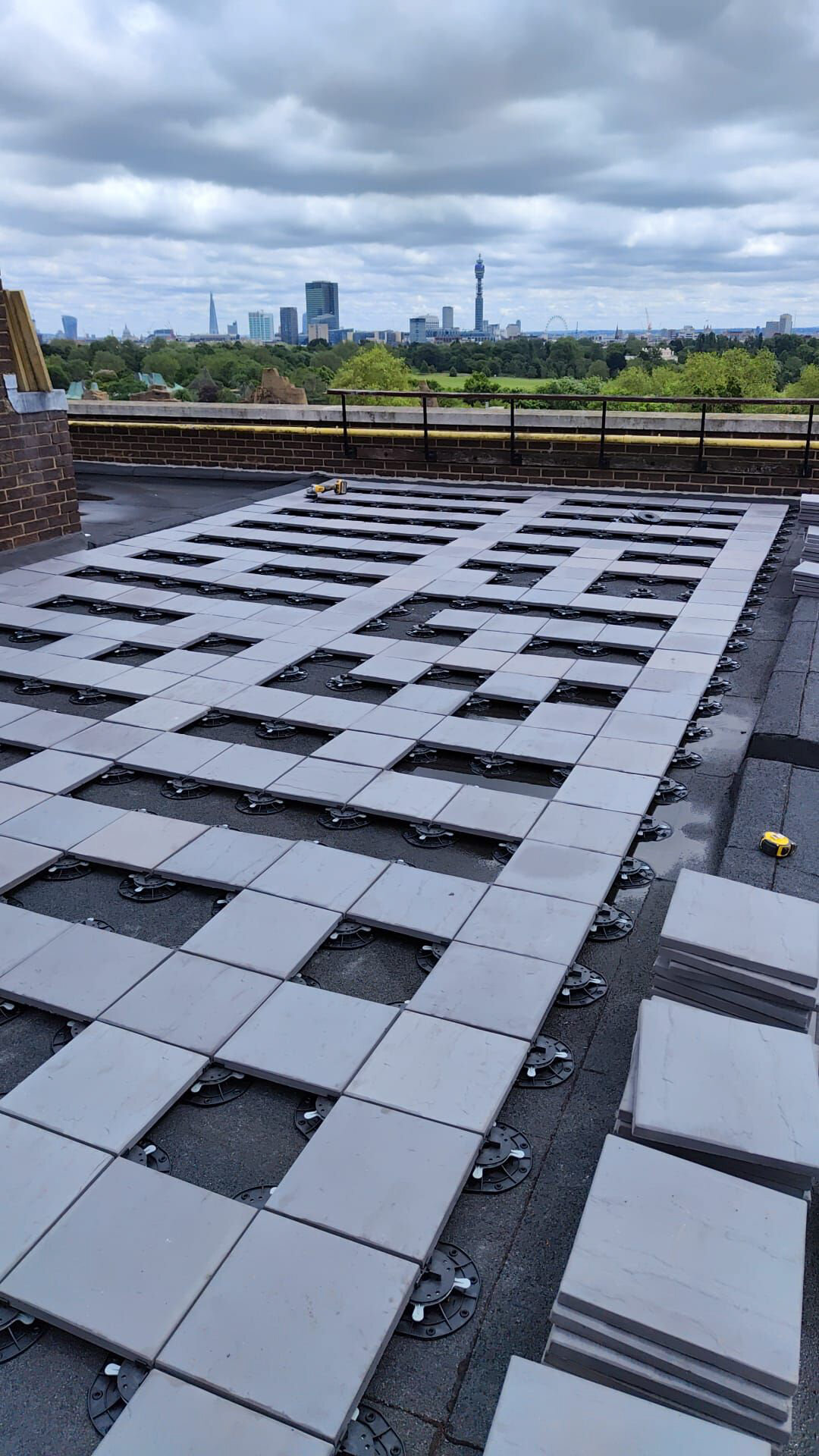 Grille de dalles de béton lourdes partiellement installées sur des plots de terrasse réglables sur le toit d'une terrasse commerciale.