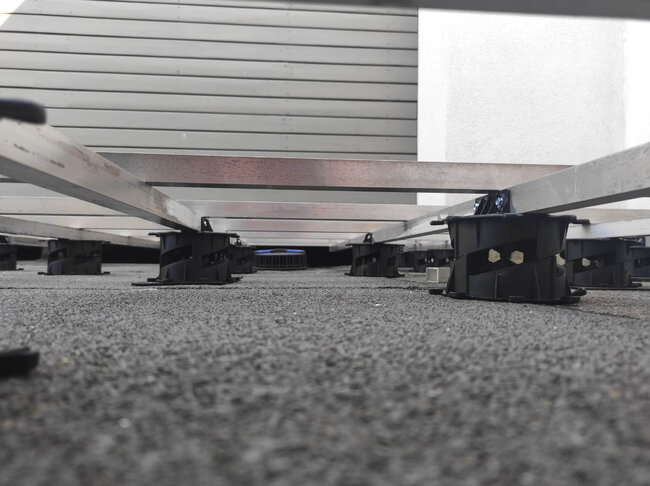 Vue en contre-plongée de lambourdes de terrasse en aluminium soutenues par des plots réglables à profil bas sur une terrasse.