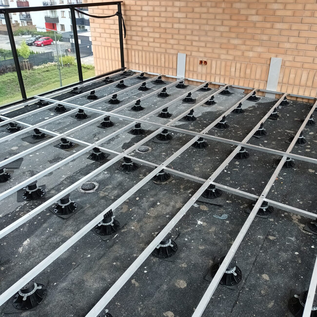 Sous-structure en grille de lambourdes aluminium soutenue par des plots réglables sur une terrasse surélevée.