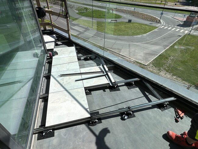 Vue de dessus d'une installation de plancher surélevé de balcon avec des dalles en porcelaine sur des lambourdes en aluminium et des plots réglables en plastique.