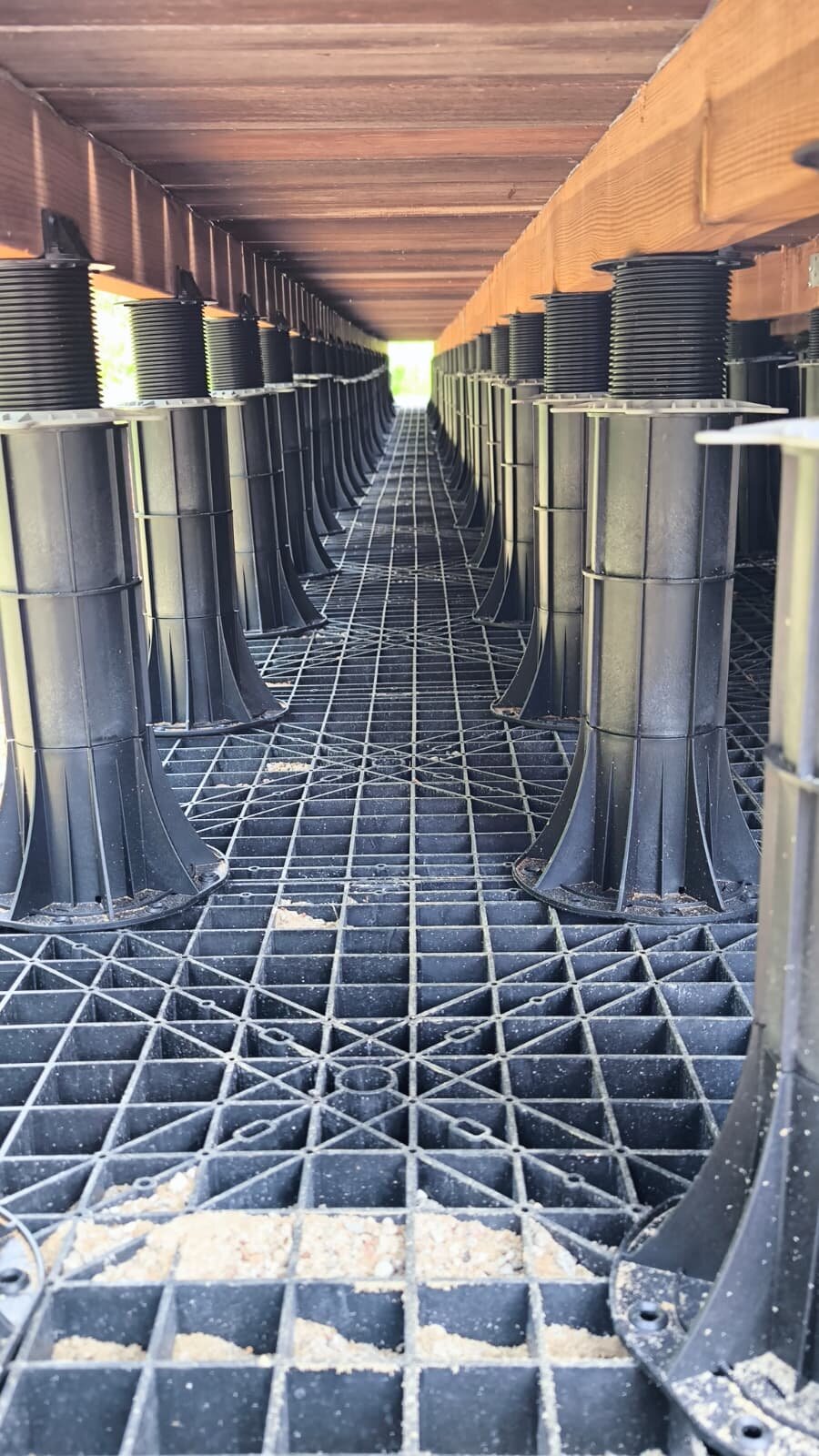 Système de plots réglables en plastique installé sous une structure de terrasse sur toit.