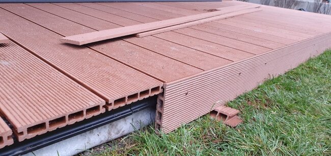 Lames composites à âme creuse avec habillage de finition installées lors de la construction d'une terrasse extérieure.