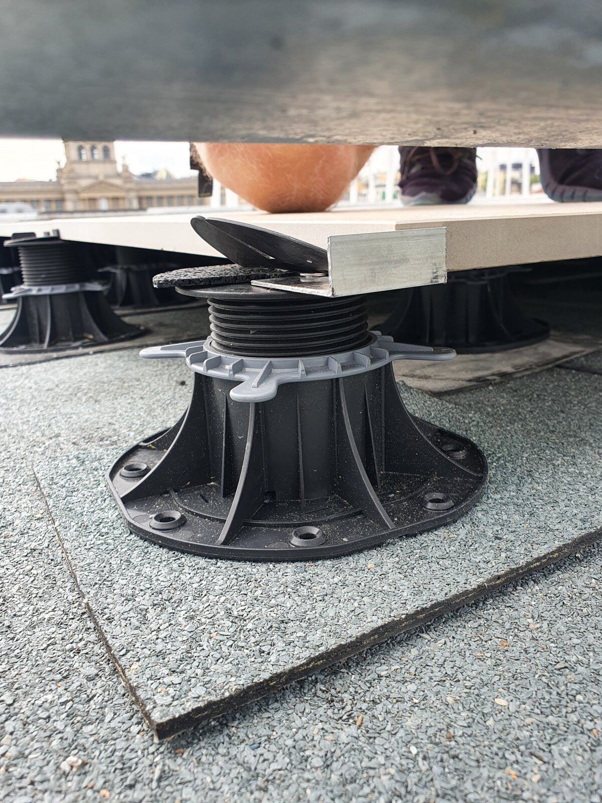 Close-up of an adjustable plastic pedestal support under a raised terrace paver tile.