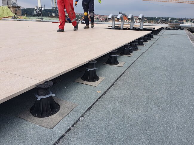 Ouvriers marchant sur une terrasse surélevée partiellement installée sur un toit soutenu par des plots réglables.