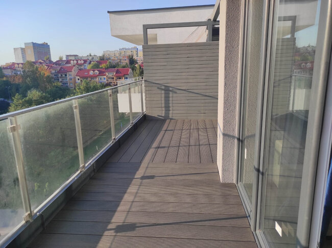 Balcon d'appartement moderne avec lames composites, garde-corps en verre et cloison d'intimité.