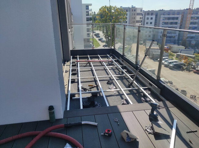 Installation de terrasse de balcon en cours de réalisation avec structure visible en lambourdes aluminium, plots réglables et lames composites.