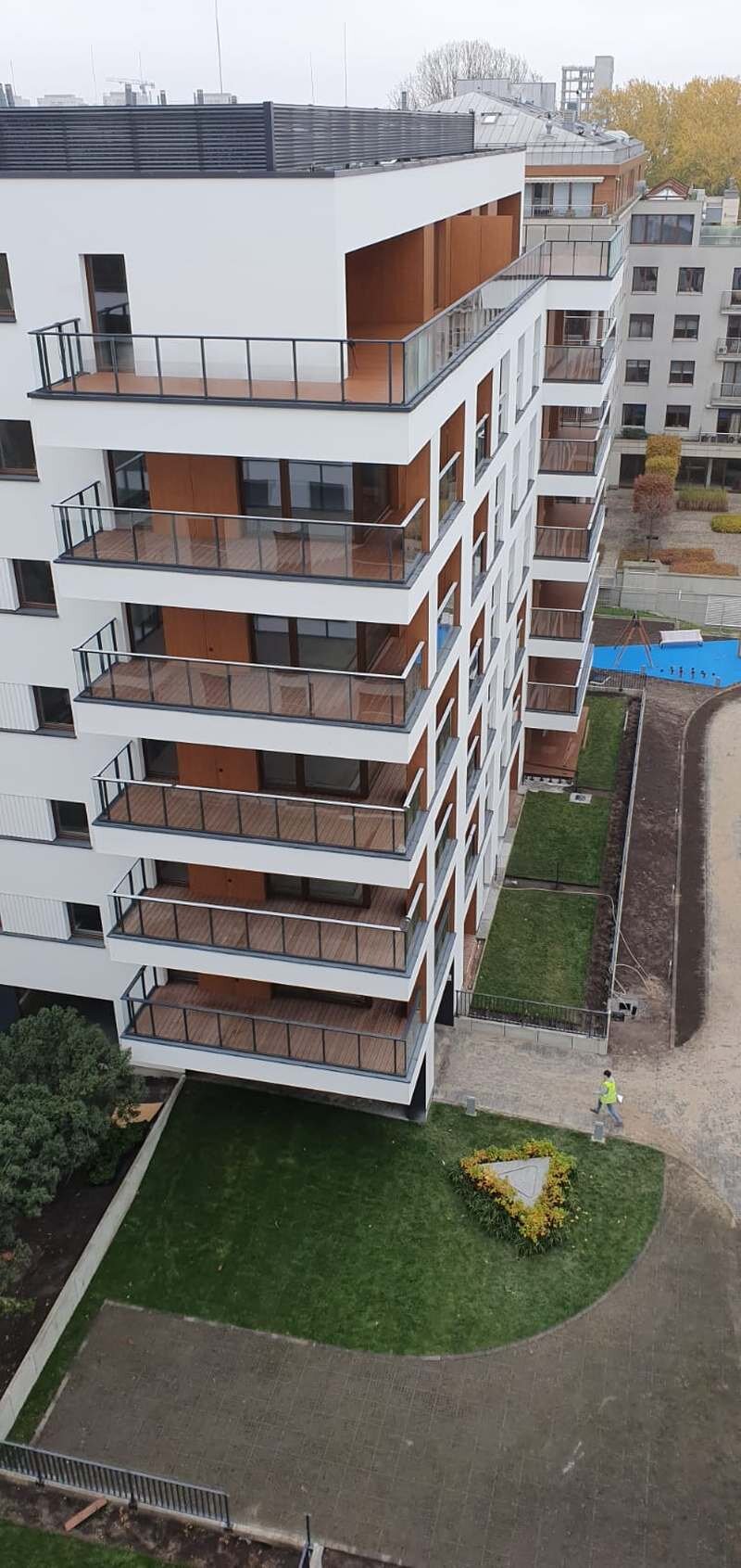 Vue extérieure d'un bâtiment résidentiel moderne à plusieurs étages avec des balcons finis en bois et des garde-corps en verre.