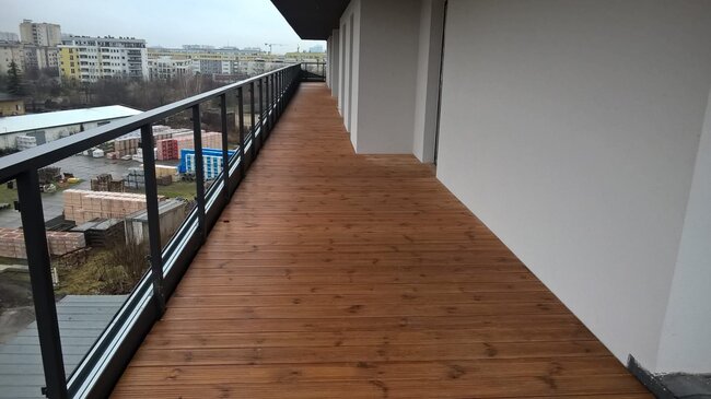 Terrasse en bois surélevée sur un long balcon d'appartement avec garde-corps en verre et en acier.