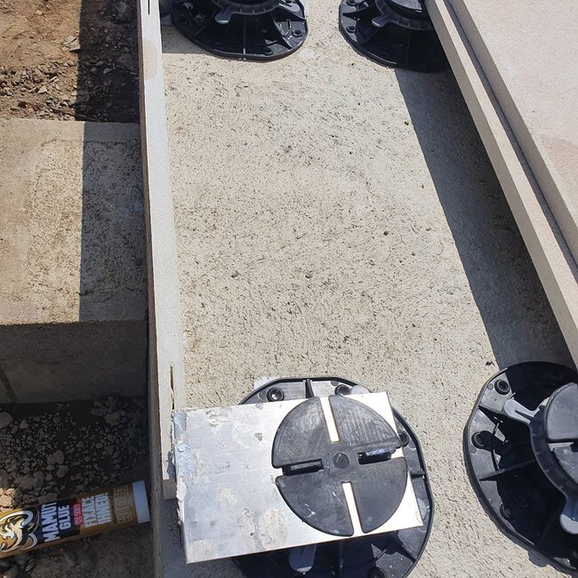 Système de plots réglables pour le support de dalles installé sur un support béton.