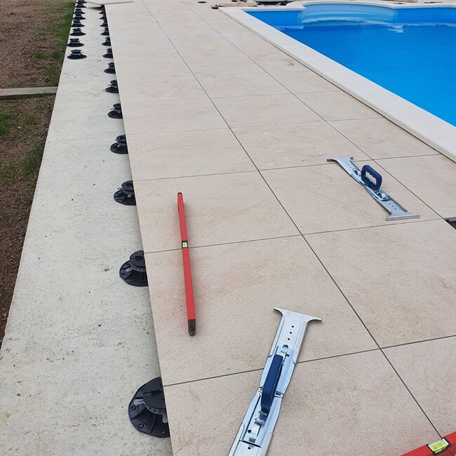 Installation de dalles en grès cérame sur plots réglables autour d'une piscine.