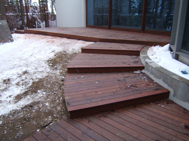 Marches de terrasse en bois courbées menant à une terrasse extérieure entourée de neige en hiver.