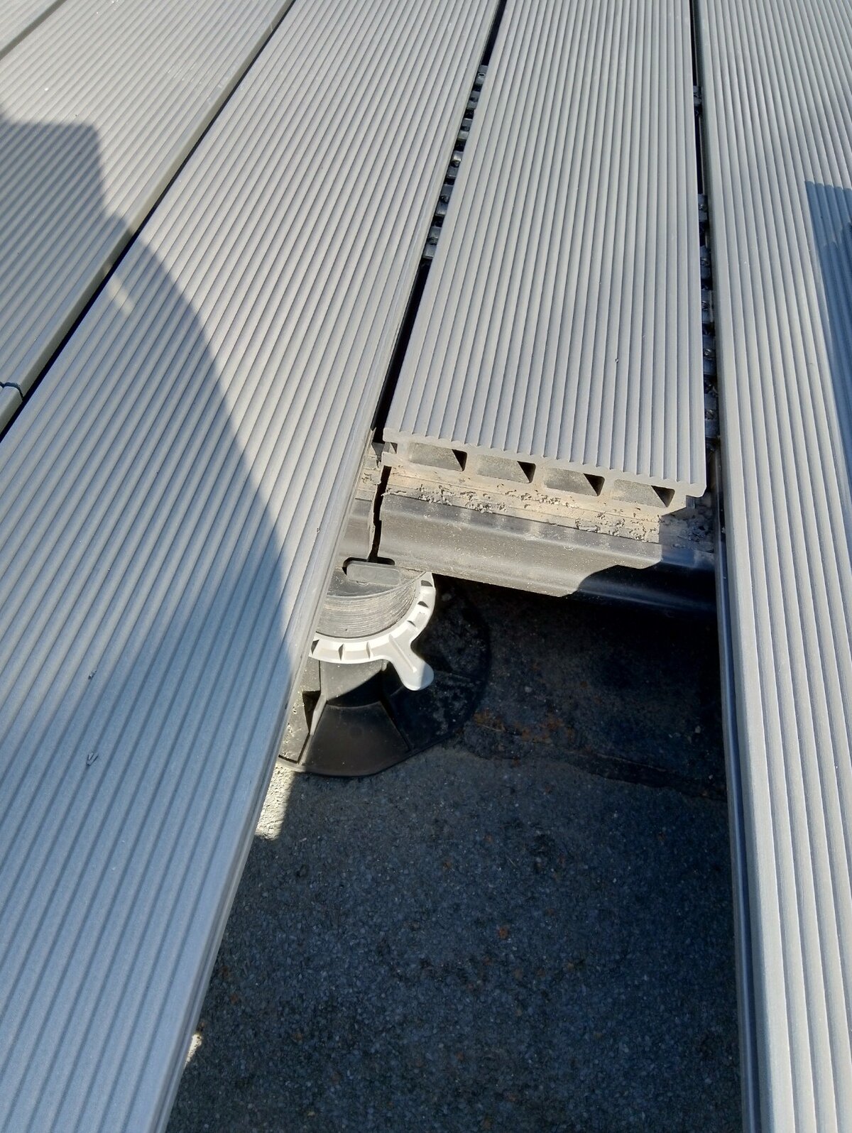 Gros plan de lames de terrasse composites grises rainurées installées sur un plot de terrasse réglable.