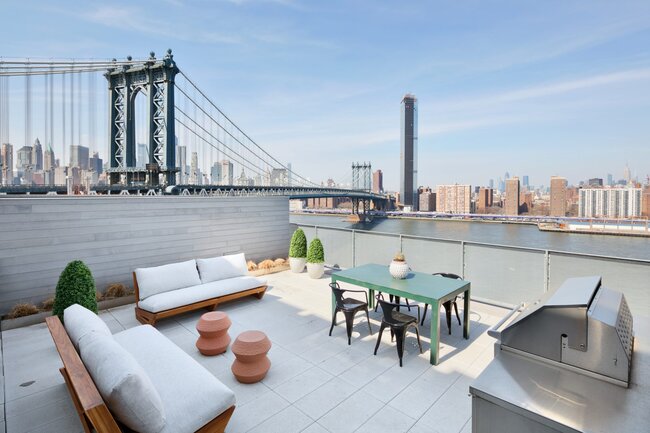 Terrasse surélevée sur le toit avec mobilier d'extérieur, grill et vue sur le Manhattan Bridge et le panorama de New York.