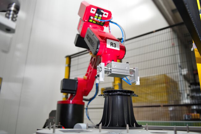 Bras robotique rouge assemblant un plot réglable noir pour terrasse dans une usine automatisée.