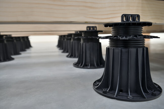 Lambourdes de terrasse en bois soutenues par des plots réglables en plastique noir.