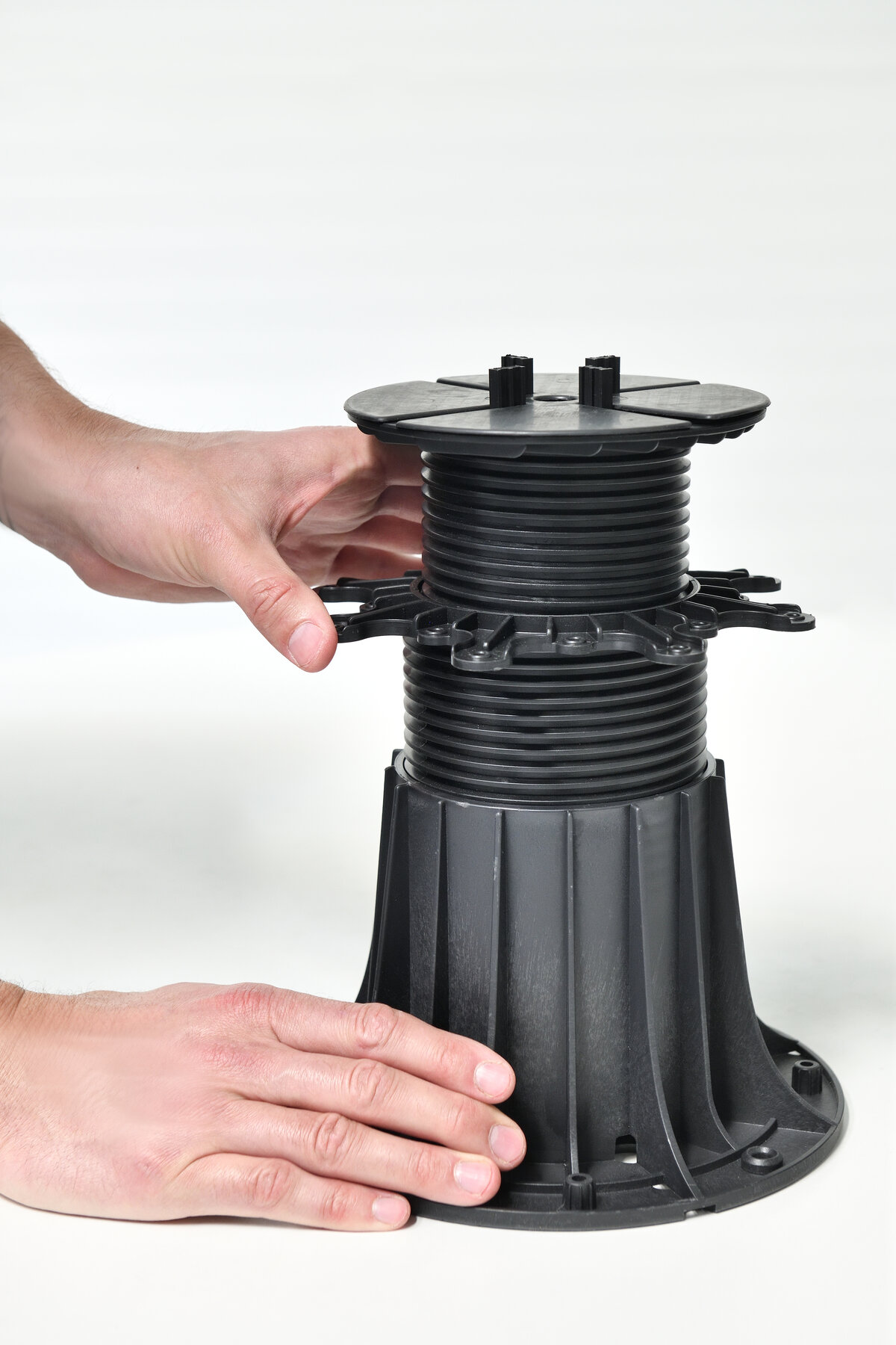 Mains réglant la hauteur d'un plot en plastique noir pour dalles de terrasse.