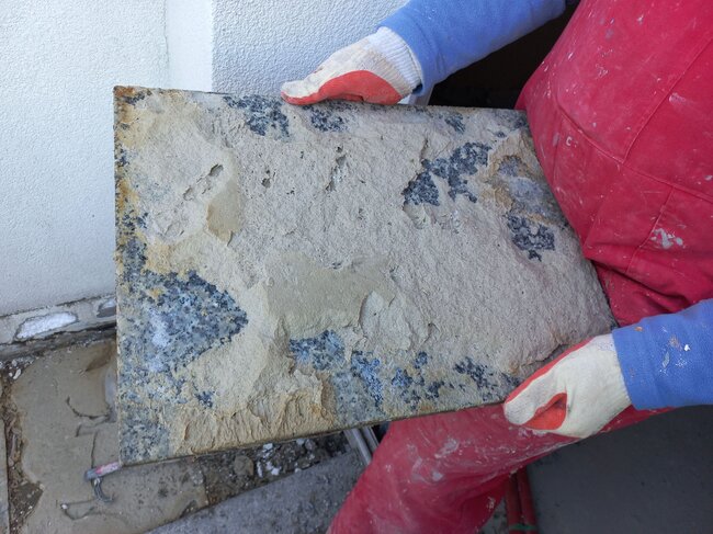 Ouvrier tenant une dalle en granit endommagée avec des restes de mortier-colle sur le dessous.