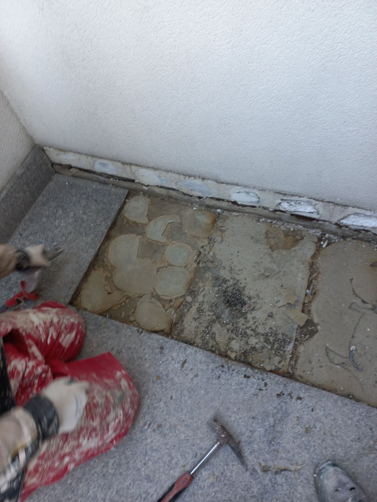 Ouvrier retirant des dalles de pierre endommagées et du mortier-colle lors de la réparation d'une terrasse.