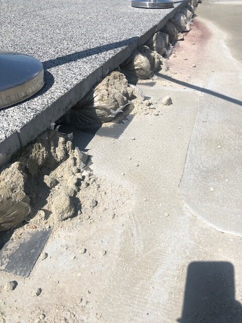 Dalles de terrasse en granit soutenues par des sacs de mortier en dessous le long du bord extérieur.