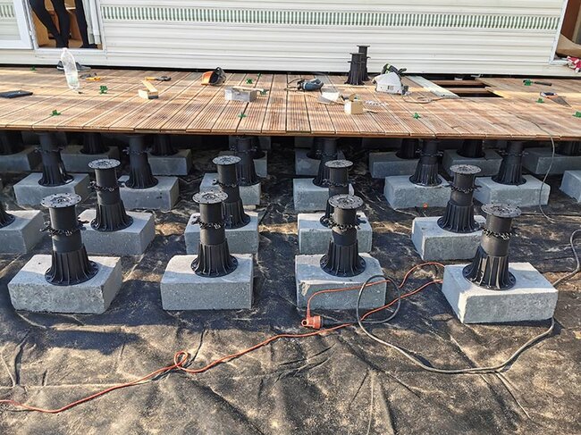 Plots réglables de terrasse montés sur des blocs de béton soutenant une structure de terrasse en bois.