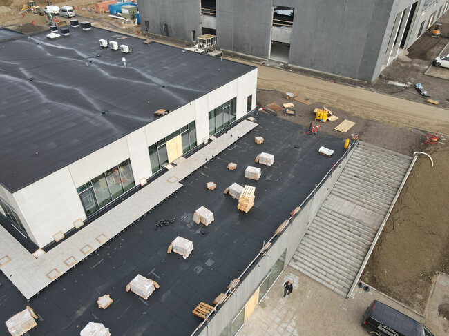 Vue aérienne d'un toit plat de bâtiment en cours de construction avec des dalles de terrasse et des plots en cours d'installation.