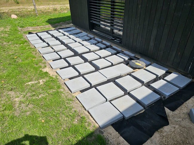 Dalles de béton carrées disposées sur un géotextile pour préparer la base d'une terrasse extérieure.