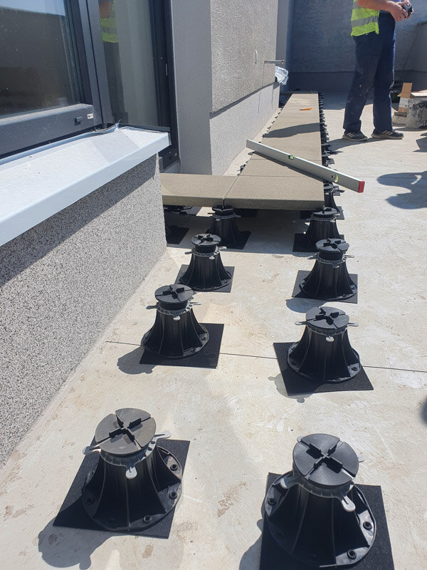 Adjustable pedestal system aligned on a concrete terrace for raised paver tile installation.