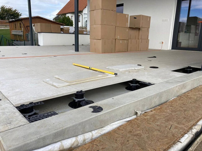 Pose de dalles sur une terrasse surélevée à l'aide de plots réglables sur un patio extérieur.