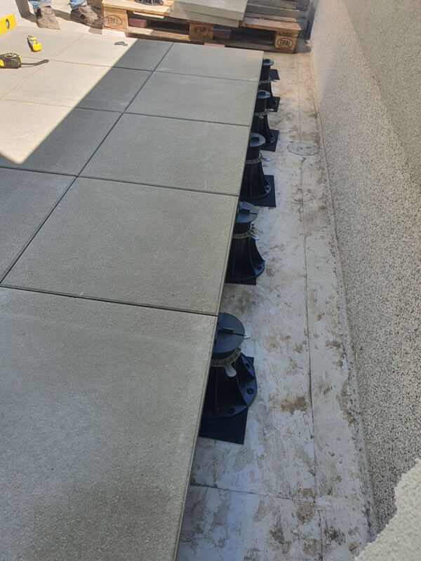 Light grey porcelain pavers supported by black adjustable pedestals during outdoor terrace raised deck installation.