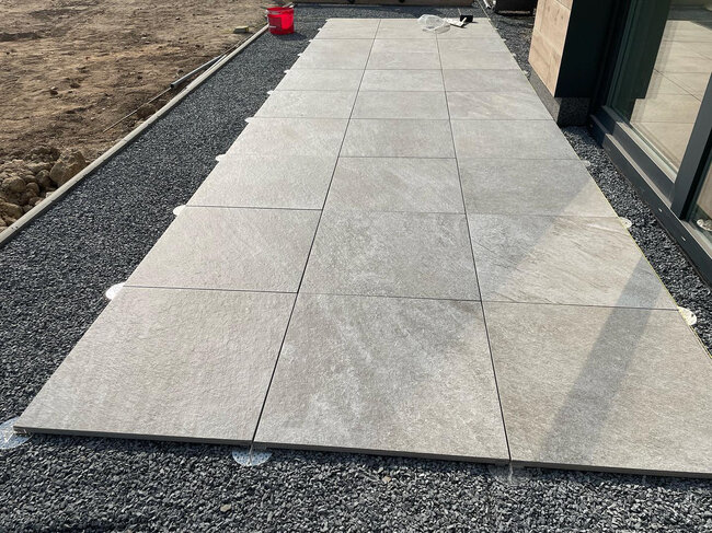 Dalles en porcelaine gris clair installées sur des plots de terrasse réglables de faible hauteur sur un lit de gravier.