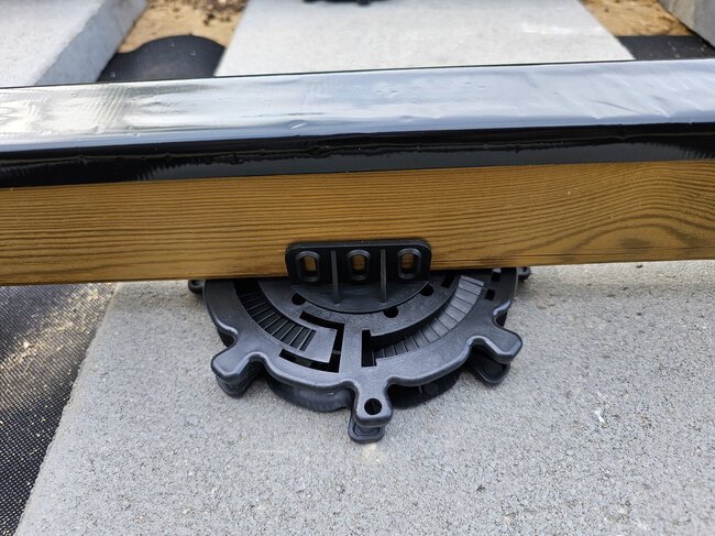 Gros plan d'un plot réglable en plastique soutenant une lambourde en bois de terrasse.