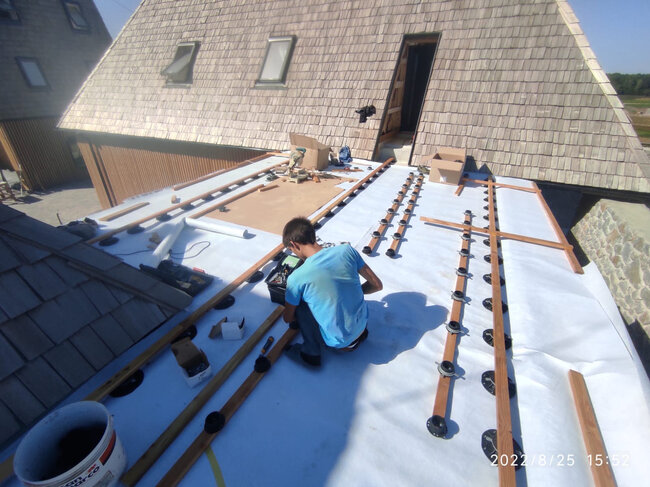 Installateur posant des plots réglables de terrasse et des lambourdes en bois sur une membrane de toit plat.